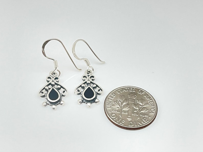 May include: A pair of silver dangle earrings with black teardrop-shaped stones. The earrings are about the size of a dime.