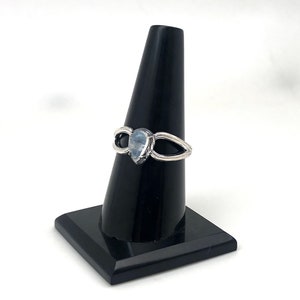 May include: A silver ring featuring a teardrop-shaped moonstone set in the centre. The ring has a delicate, open design with two curved bands that meet at the stone.