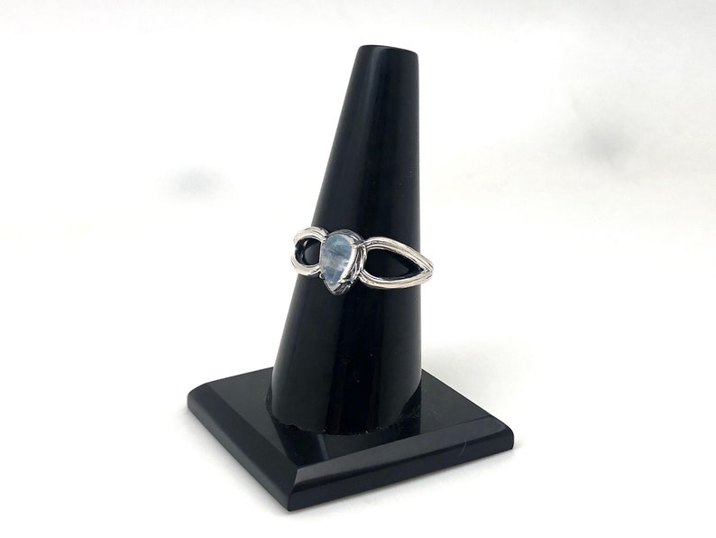 May include: A silver ring featuring a teardrop-shaped moonstone set in the centre. The ring has a delicate, open design with two curved bands that meet at the stone.