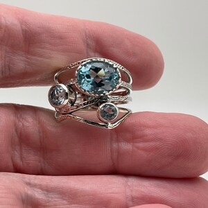 May include: A silver ring with three blue topaz gemstones. The ring has a delicate, intricate design.