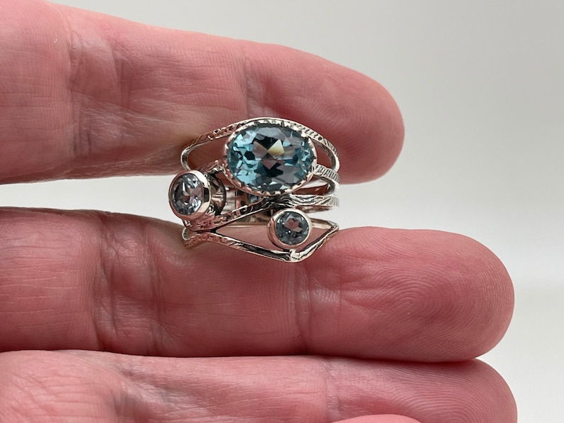 May include: A silver ring with three blue topaz gemstones. The ring has a delicate, intricate design.