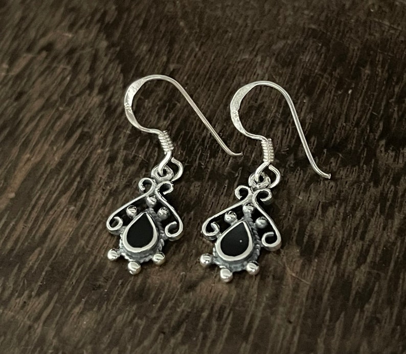 May include: A pair of silver dangle earrings with black teardrop-shaped stones. The earrings have a delicate, ornate design.