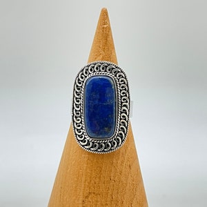 May include: A silver ring with a large, rectangular, dark blue lapis lazuli stone set in a detailed, ornate silver frame.