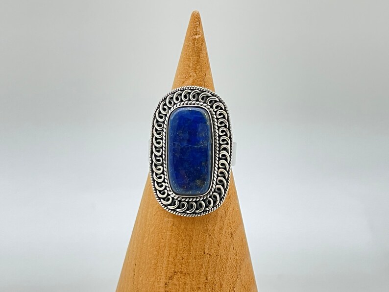 May include: A silver ring with a large, rectangular, dark blue lapis lazuli stone set in a detailed, ornate silver frame.