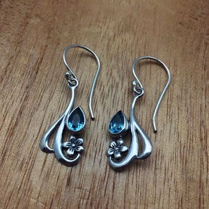 May include: A pair of silver dangle earrings featuring blue teardrop-shaped gemstones and a flower design.