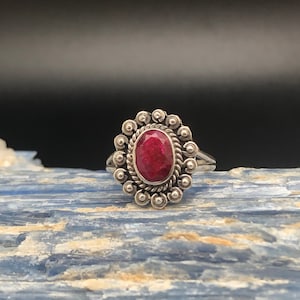 May include: A silver ring with a red ruby gemstone set in a beaded halo design.