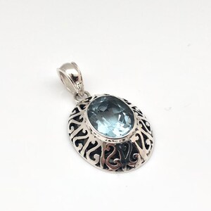 May include: A silver pendant with an oval-shaped blue gemstone set in a filigree design.