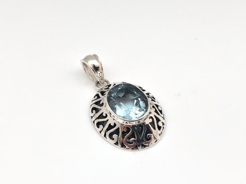 May include: A silver pendant with an oval-shaped blue gemstone set in a filigree design.