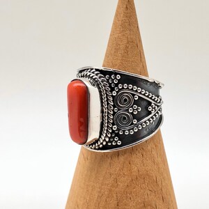 May include: A silver ring with an orange coral stone set in a wide band with intricate silver designs.