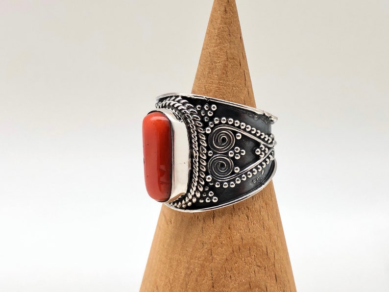 May include: A silver ring with an orange coral stone set in a wide band with intricate silver designs.