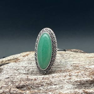 May include: A silver ring featuring an oval green gemstone set within an ornate filigree design.