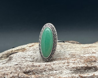 May include: A silver ring with an oval-shaped green gemstone set in a decorative filigree design.
