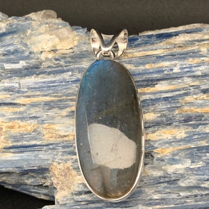 May include: A silver pendant featuring a large oval-shaped labradorite gemstone with iridescent blue and green hues. The stone is set in a silver bezel and hangs from a silver bail.