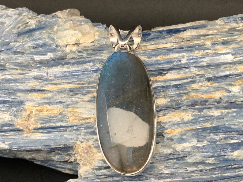 May include: A silver pendant featuring a large oval-shaped labradorite gemstone with iridescent blue and green hues. The stone is set in a silver bezel and hangs from a silver bail.