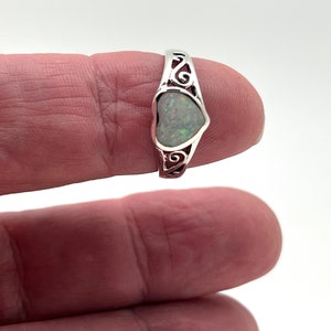 May include: A silver ring with a heart-shaped opal gemstone. The ring has a delicate, scroll-like design.