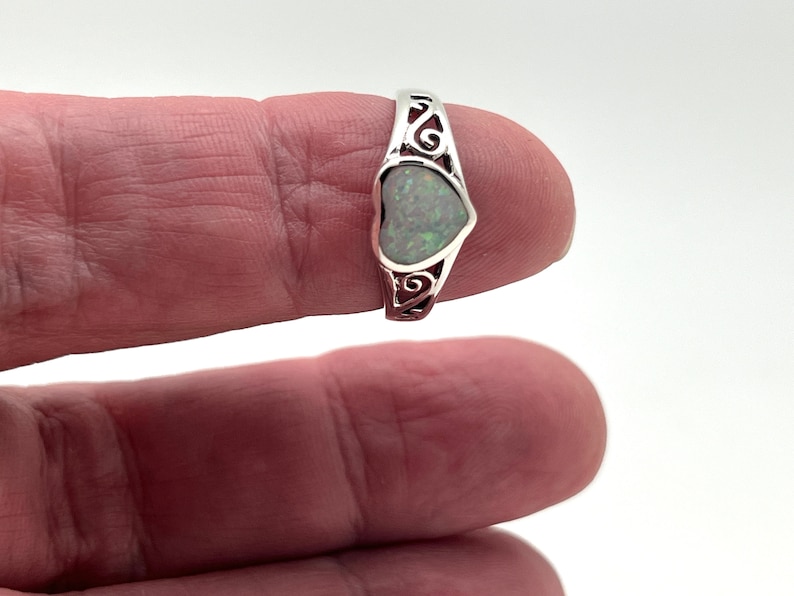 May include: A silver ring with a heart-shaped opal gemstone. The ring has a delicate, scroll-like design.