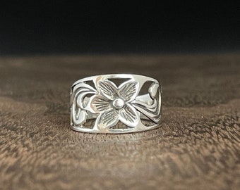 May include: A silver ring with a floral design. The ring is wide and has a cutout design of a flower with leaves.