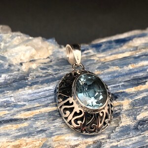 May include: A silver pendant with an oval-shaped blue topaz gemstone set in a filigree design.