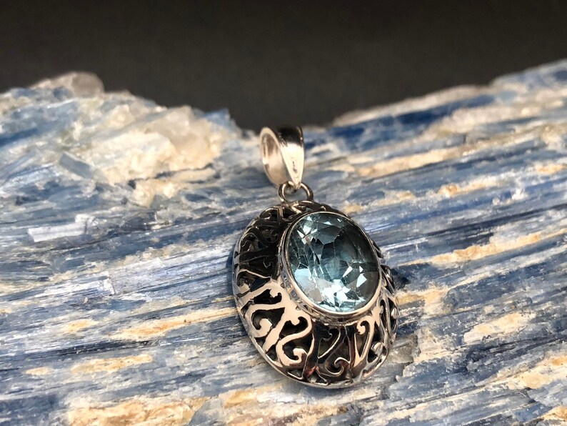 May include: A silver pendant with an oval-shaped blue topaz gemstone set in a filigree design.