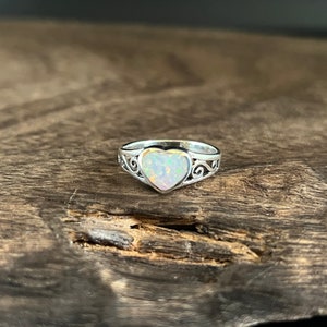 May include: A silver ring with a heart-shaped opal gemstone. The ring has a delicate, ornate design.