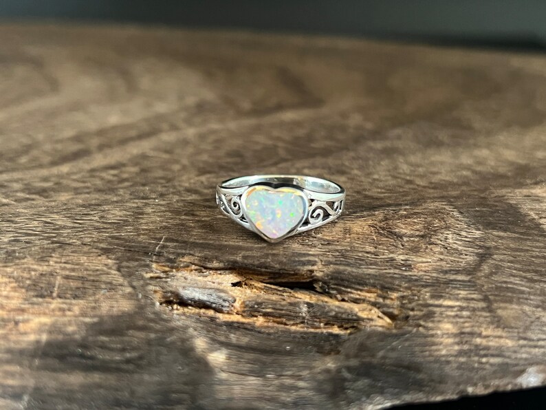 May include: A silver ring with a heart-shaped opal gemstone. The ring has a delicate, ornate design.