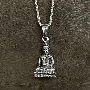 Puede incluir: Un collar de cadena de plata con un colgante de plata que presenta una representación detallada de un Buda sentado.
