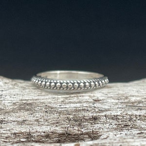 May include: A silver ring with a beaded design. The ring is simple and elegant.