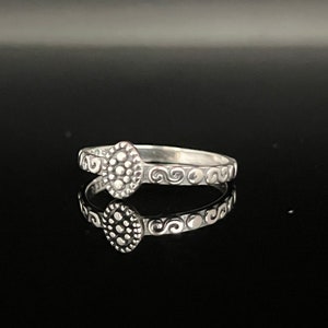 May include: A silver ring with a textured, circular design in the center and a swirl pattern around the band.