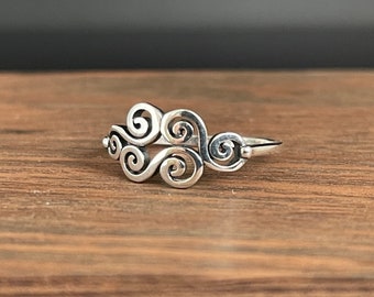 May include: A silver ring featuring a swirling design, reminiscent of clouds or waves.