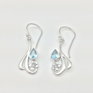 May include: Silver dangle earrings featuring a blue teardrop gemstone and a floral design.