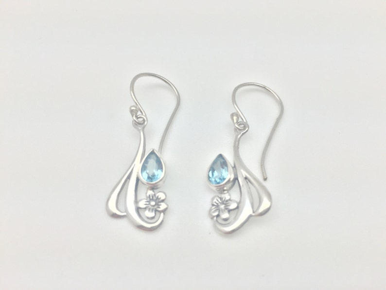 May include: Silver dangle earrings featuring a blue teardrop gemstone and a floral design.