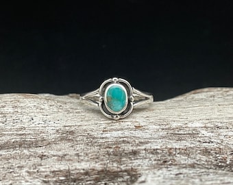 May include: A silver ring with a turquoise stone set in a decorative oval bezel. The ring has a delicate design with a split band.