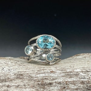 May include: A silver ring with three blue topaz gemstones. The ring has a textured band and a delicate design.