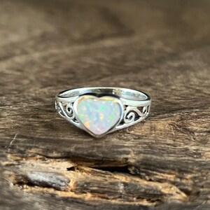 May include: A silver ring with a heart-shaped opal gemstone. The ring has a delicate, ornate design.