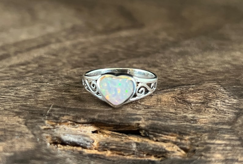 May include: A silver ring with a heart-shaped opal gemstone. The ring has a delicate, ornate design.