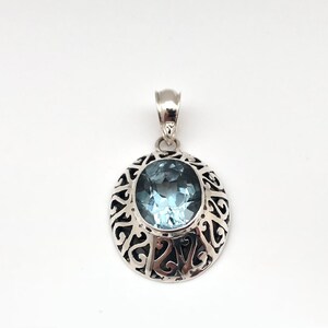 May include: A silver pendant with an oval-shaped blue topaz gemstone set in a filigree design.