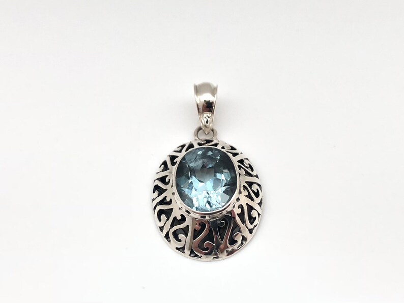 May include: A silver pendant with an oval-shaped blue topaz gemstone set in a filigree design.
