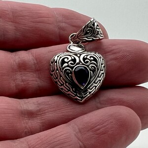 May include: A silver heart-shaped pendant with an intricate design and a purple gemstone in the center.