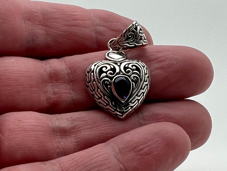 May include: A silver heart-shaped pendant with an intricate design and a purple gemstone in the center.