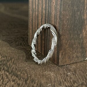 May include: A silver ring with a twisted, textured design. The ring is made of metal and has a polished finish.