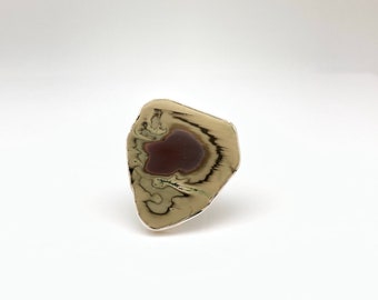 Op de afbeelding: Een zilveren ring met een unieke, onregelmatig gevormde steen. De steen is lichtbruin van kleur met een donkerbruin centrum.