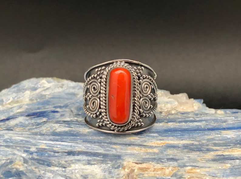 May include: A silver ring with an orange coral stone set in a detailed design.