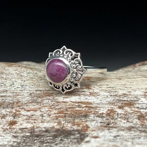 May include: A silver ring with a purple gemstone set in a filigree design.