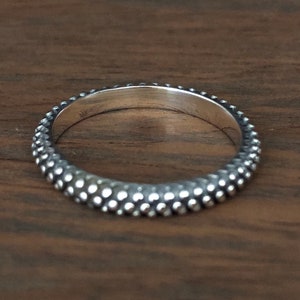 Puede incluir: Un anillo de plata con una superficie texturizada y punteada.