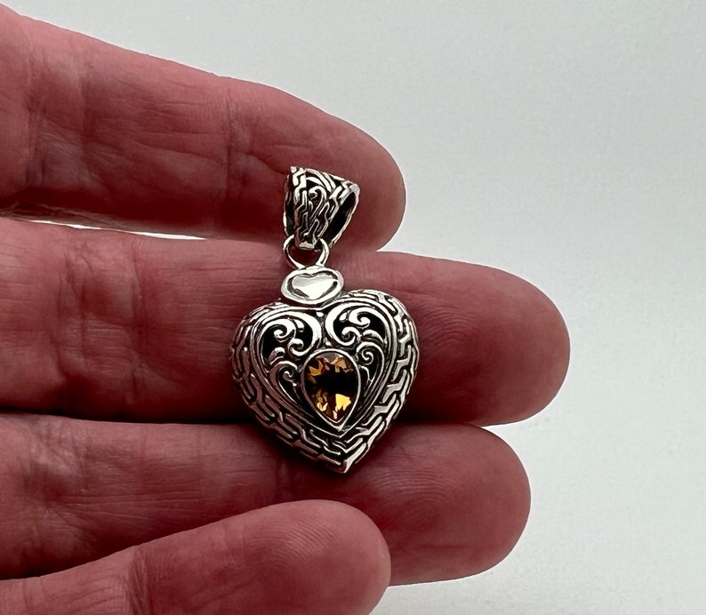 Puede incluir: Colgante de coraz&oacute;n de plata con un intrincado dise&ntilde;o de filigrana y una piedra preciosa de topacio dorado en el centro.