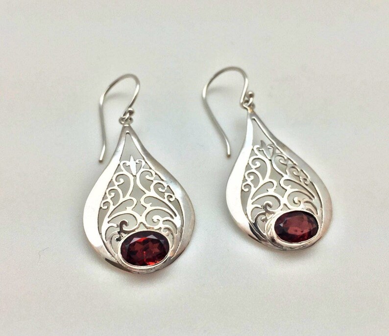 Puede incluir: Un par de pendientes de filigrana de plata con acentos de piedras preciosas rojas. Los pendientes tienen forma de l&aacute;grima y presentan un dise&ntilde;o delicado e intrincado.