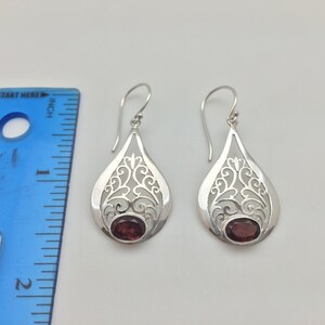 Puede incluir: Pendientes de filigrana de plata con una piedra preciosa roja en el centro. Los pendientes miden aproximadamente 2,5 cm de largo.