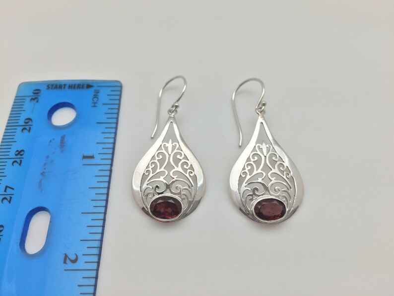 Puede incluir: Pendientes de filigrana de plata con una piedra preciosa roja en el centro. Los pendientes miden aproximadamente 2,5 cm de largo.