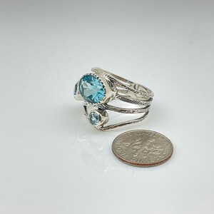 May include: A silver ring with three blue topaz gemstones. The ring has a textured band and is set with a larger oval-shaped stone and two smaller round stones.