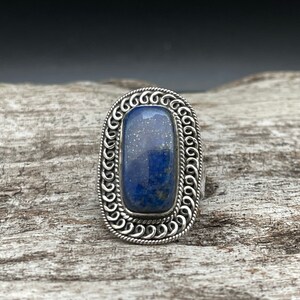 May include: A silver ring with a blue lapis lazuli stone set in a decorative, ornate silver bezel.